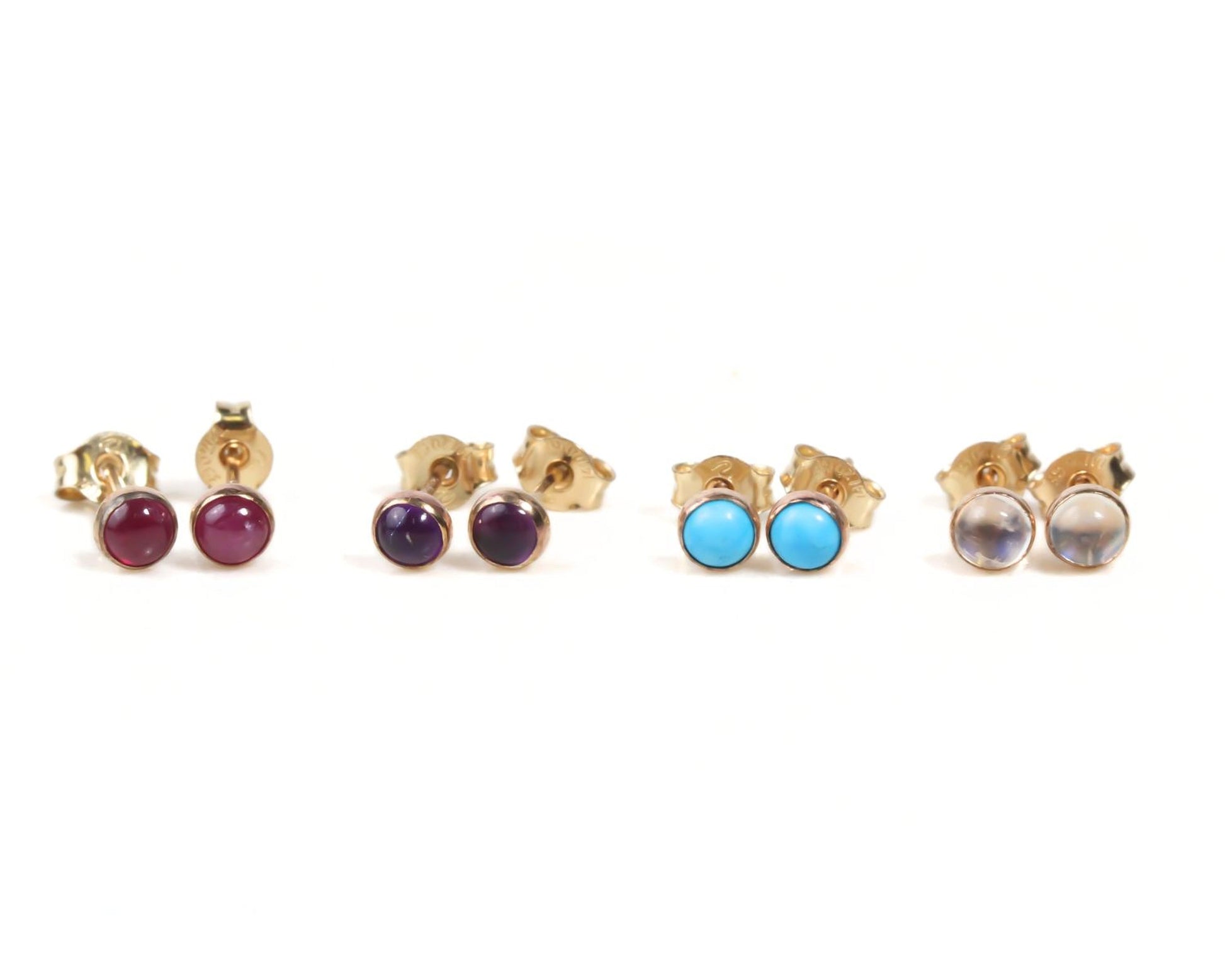 A collection of four gold-colored earrings with different colored gemstones, including red, purple, blue, and clear stones, arranged in a row.