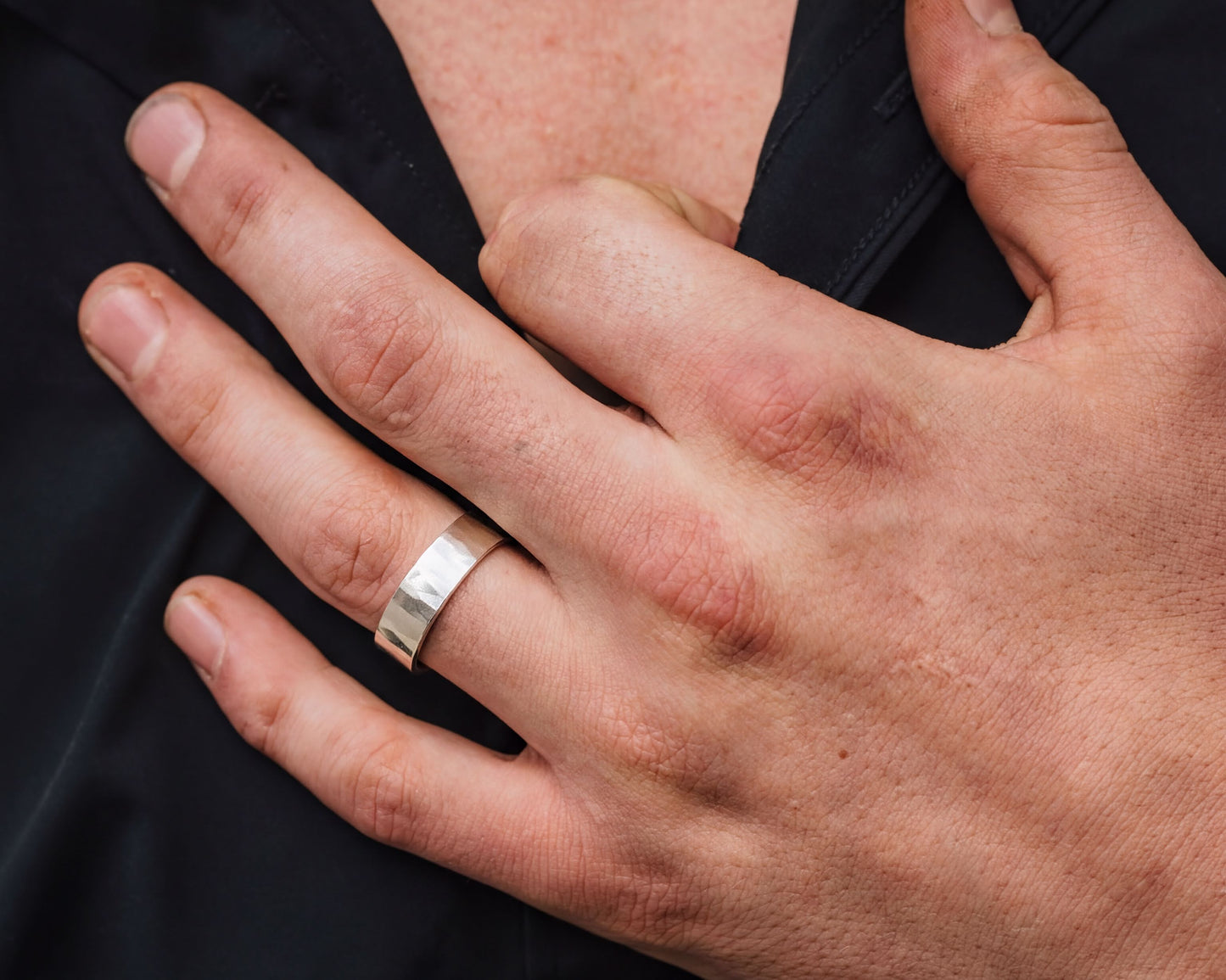 A close-up image of a person's hand wearing a silver ring, with the ring visible on the ring finger.