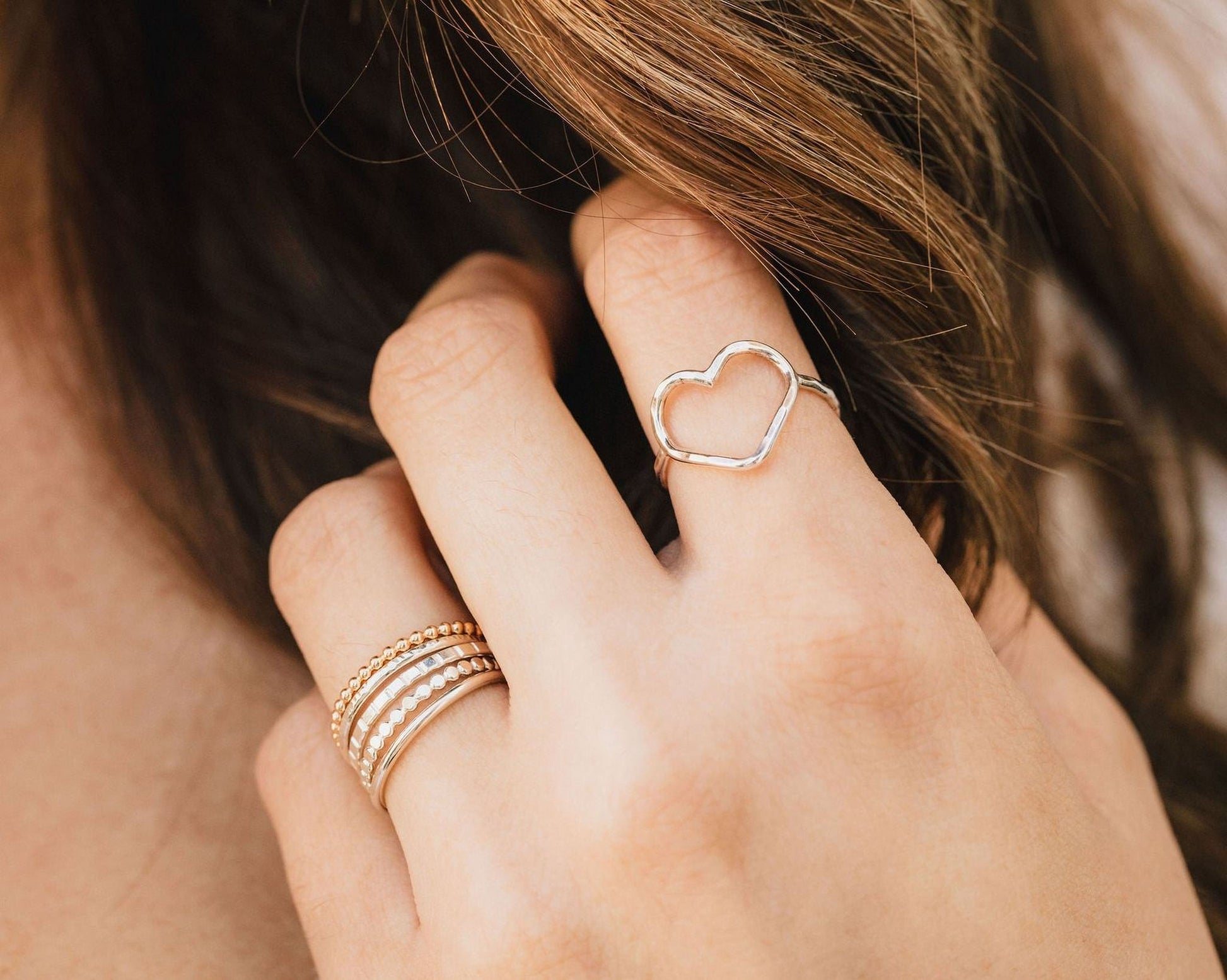 A close-up of a person's hand wearing multiple rings, including a heart-shaped ring and a stack of rings.