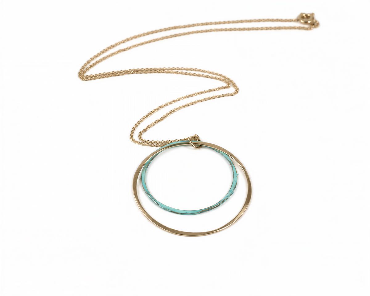 A gold necklace with a circular pendant featuring two concentric rings of different colors.