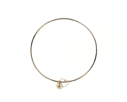 A gold-colored bangle bracelet with a charm attached to it.