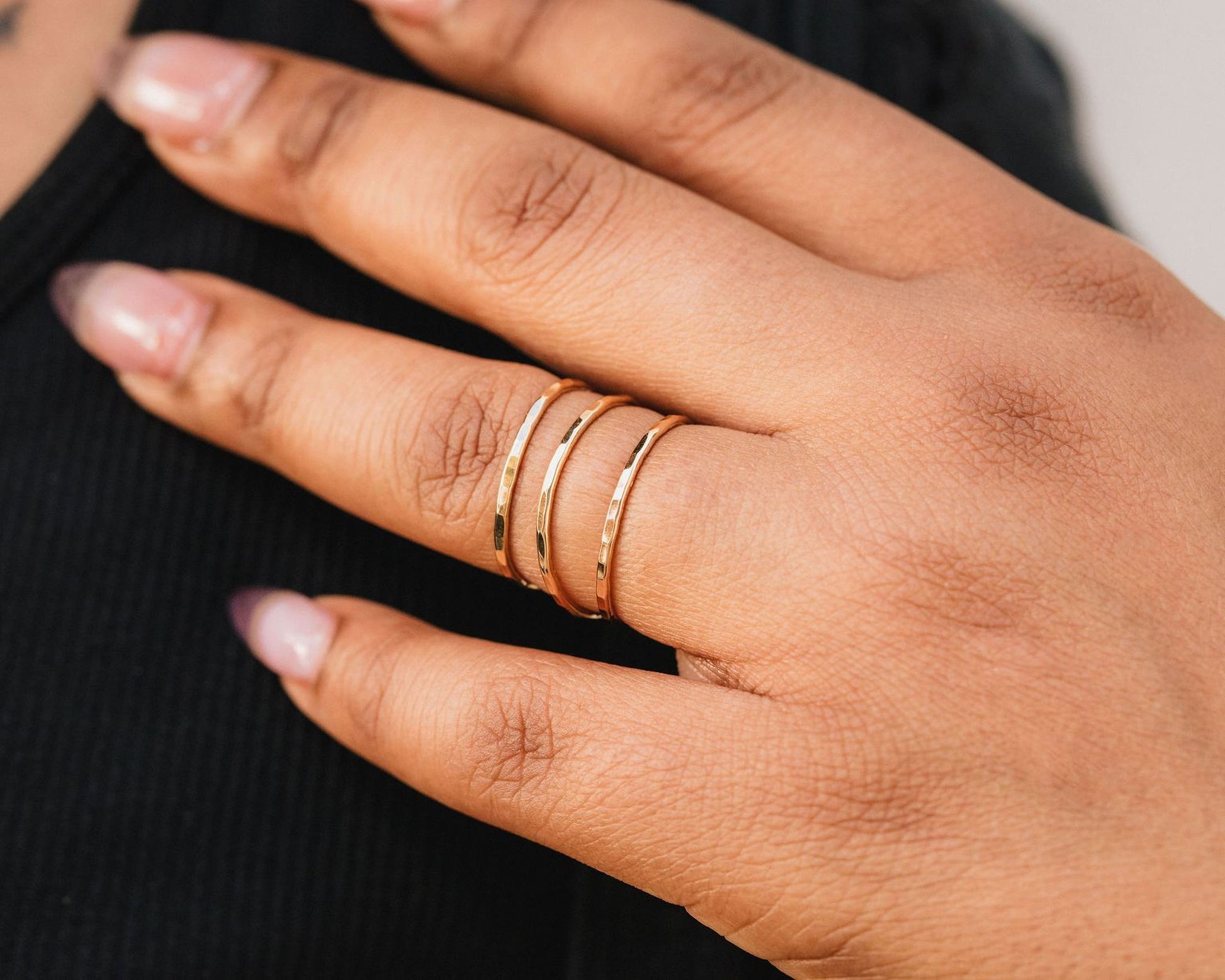 A close-up of a person's hand wearing three rings on the fingers.