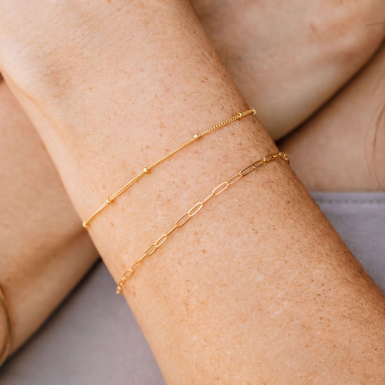 A close-up view of a person's arm wearing two gold-colored bracelets.