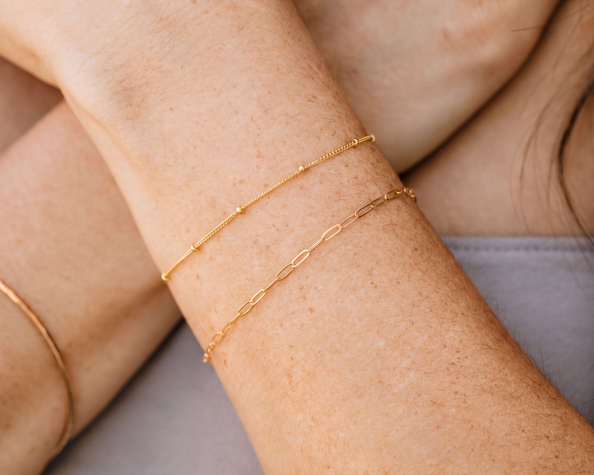 A close-up view of a person's arm wearing two gold-colored bracelets.