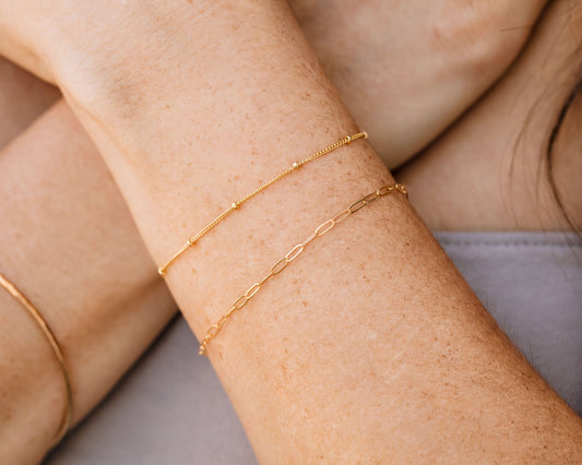 A close-up view of a person's arm wearing two gold-colored bracelets.