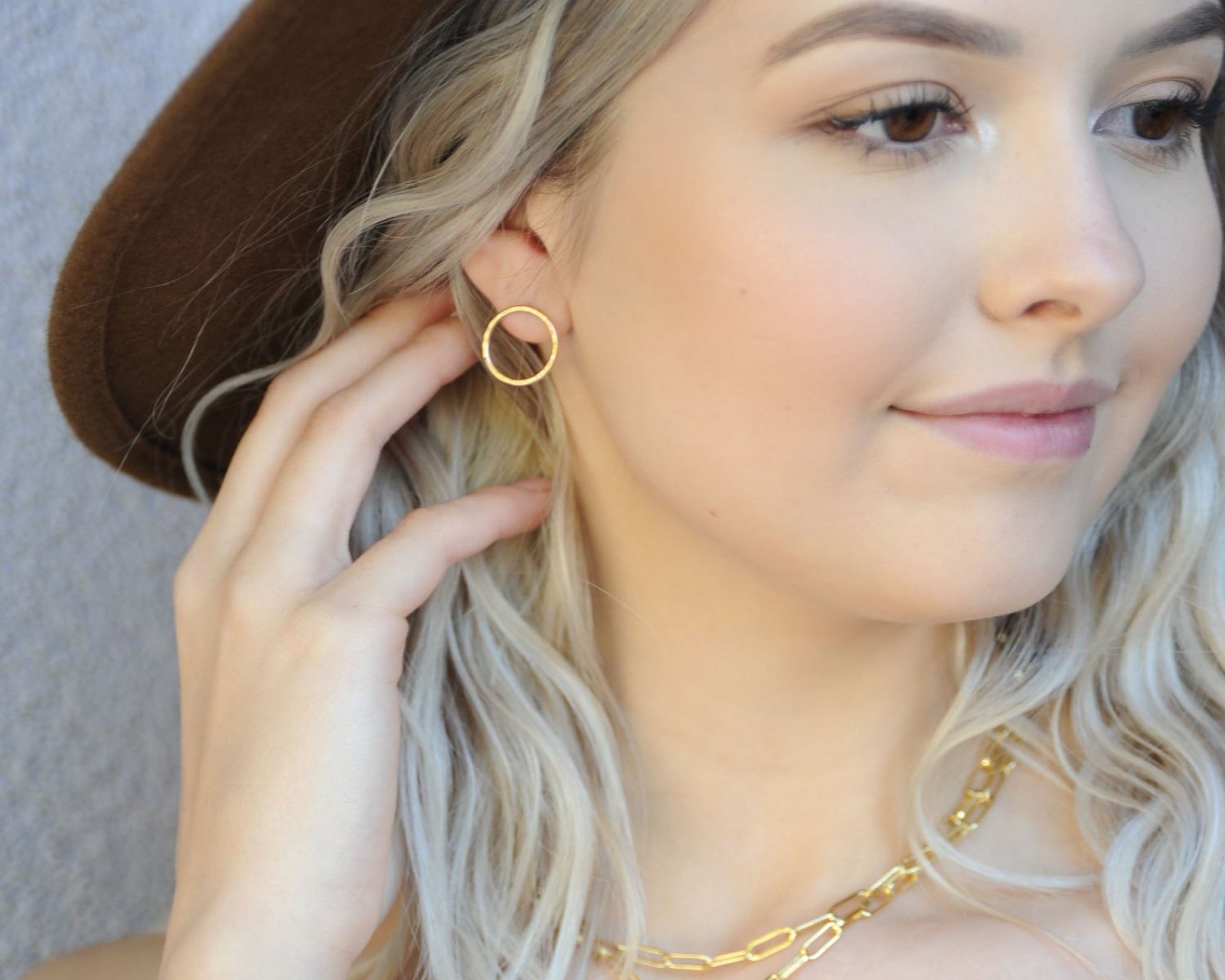 A close-up of a woman's face, with her hand touching her ear and a gold necklace visible.