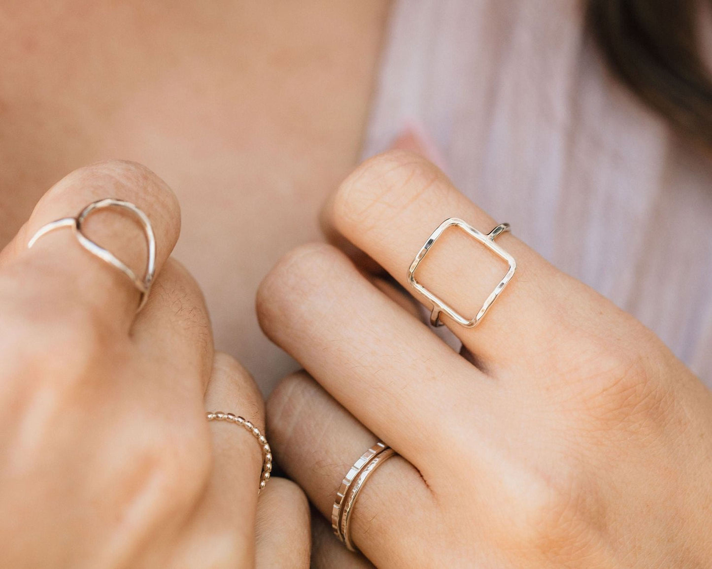 A close-up of a person's hand wearing multiple rings, including a square ring and several smaller rings on the fingers.