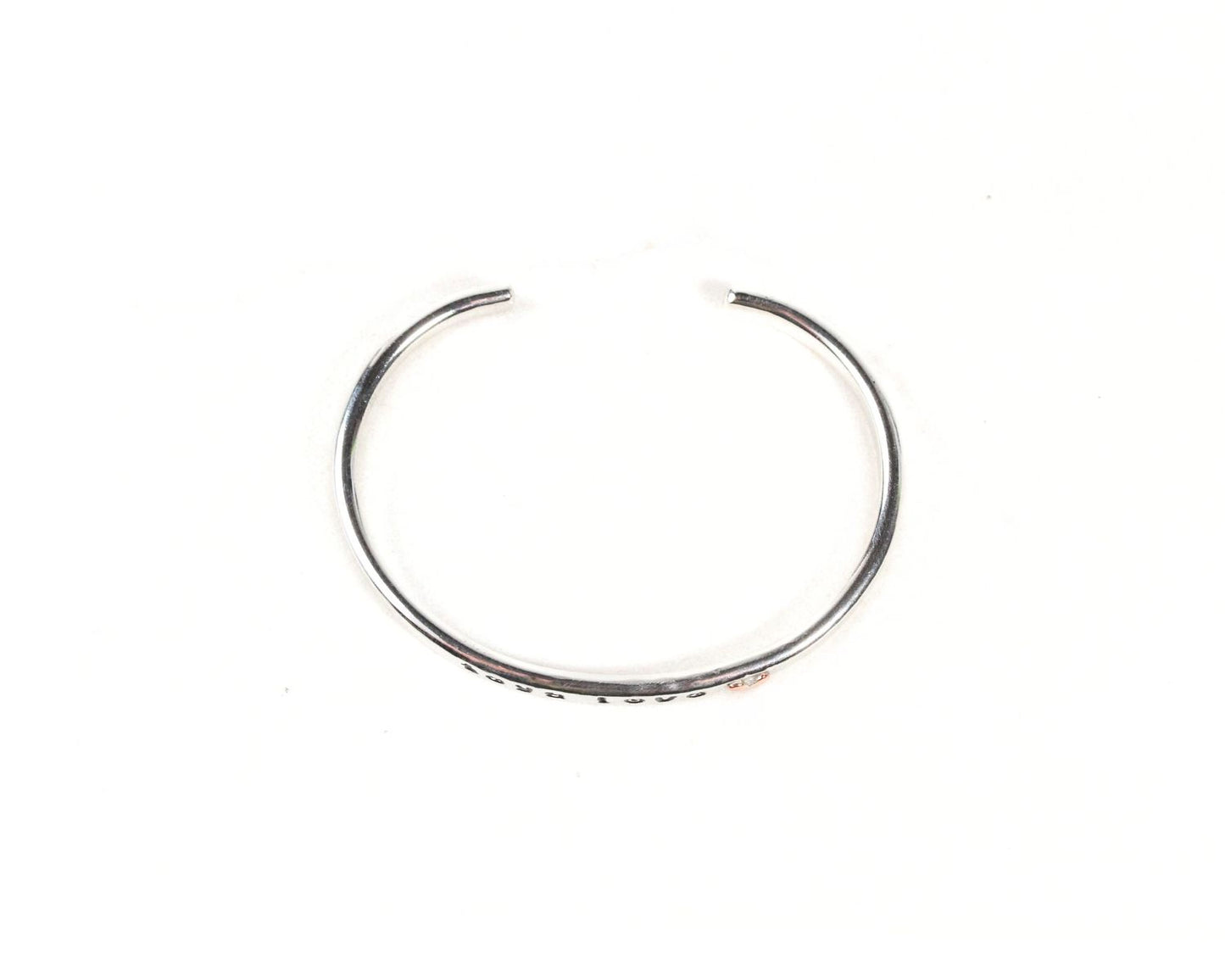 A silver-colored bracelet with a curved design, placed against a white background.