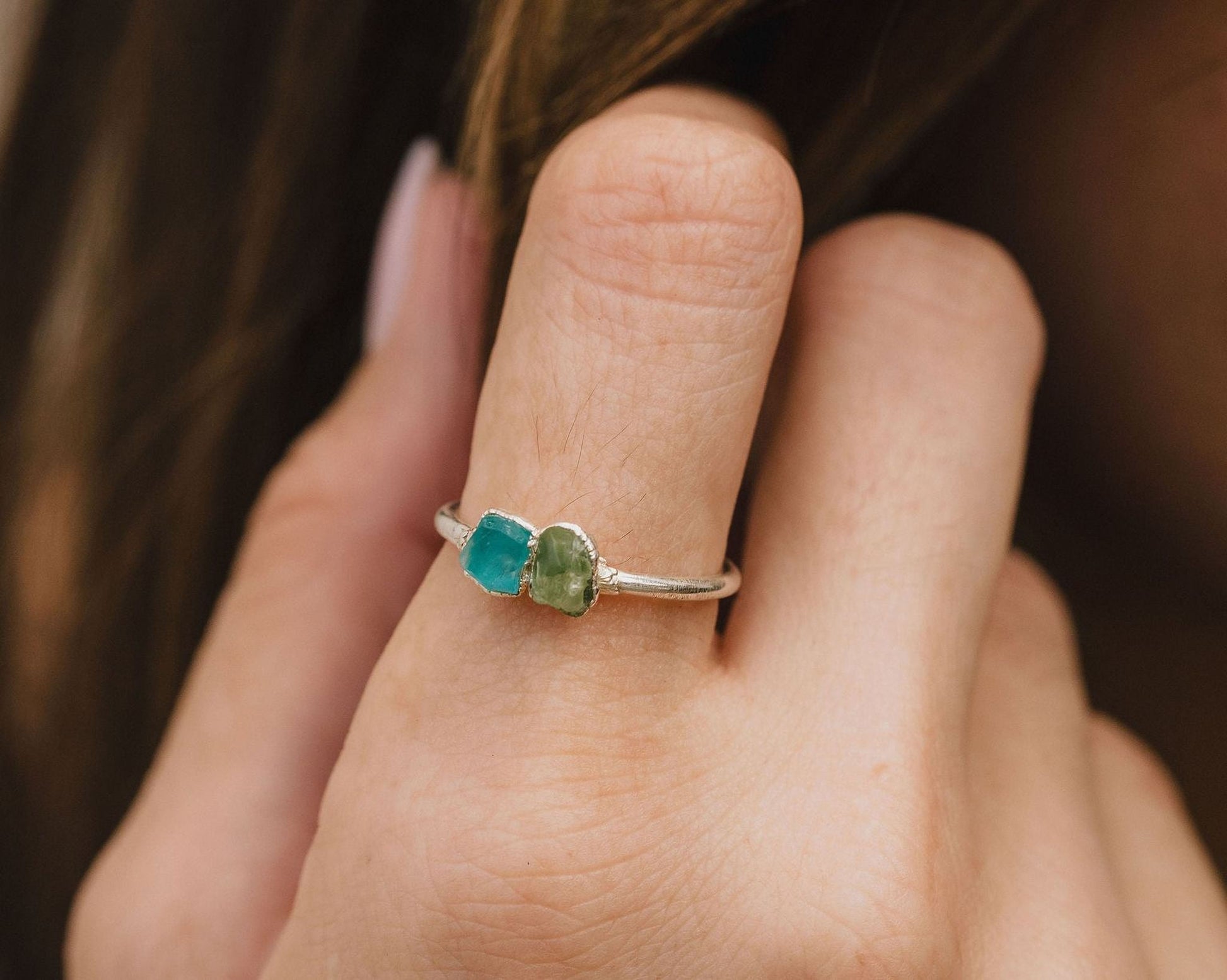 A close-up of a person's hand wearing a silver ring with two green gemstones.