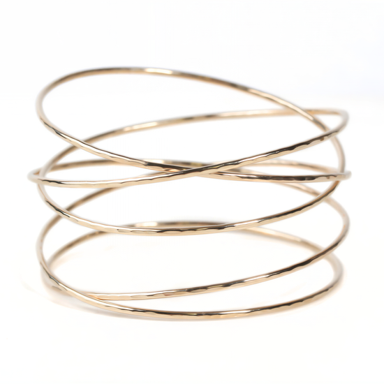A gold-colored bracelet with multiple overlapping rings, creating a layered and textured appearance.