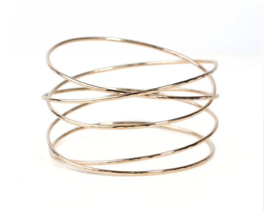 A gold-colored bracelet with multiple overlapping rings, creating a layered and textured appearance.