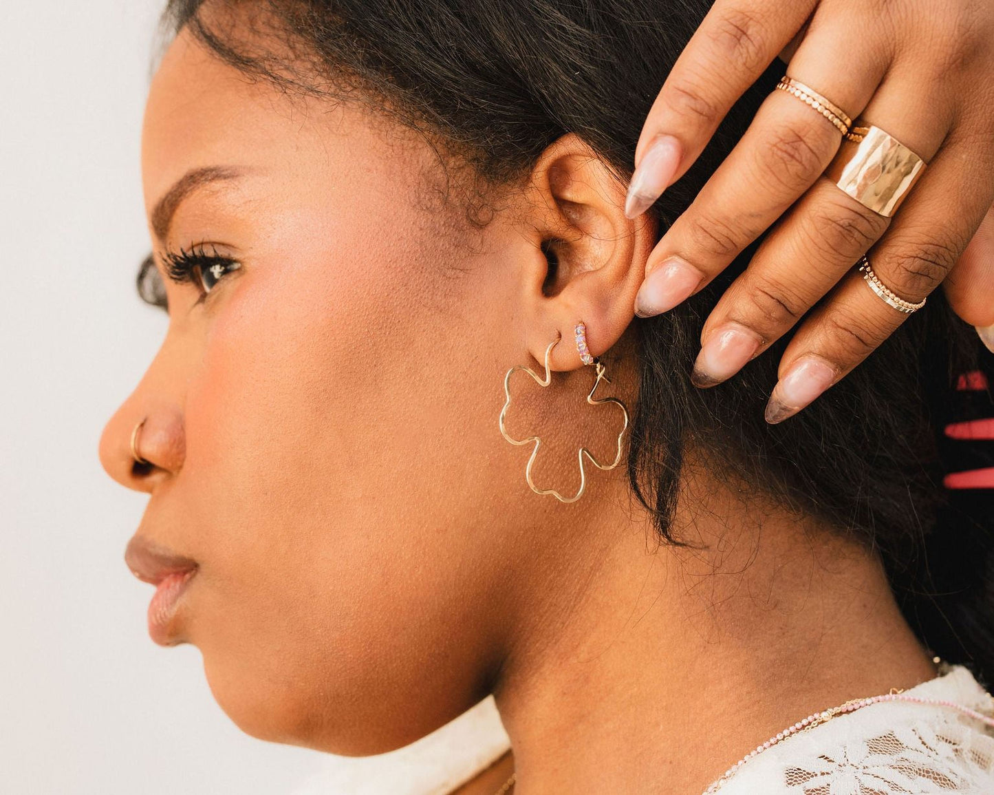 A close-up of a woman's face, with her hands gently touching her ear and her fingers adorned with multiple rings.