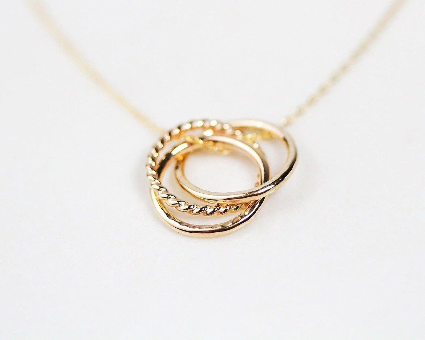 A close-up image of a gold necklace with a pendant featuring three intertwined rings.