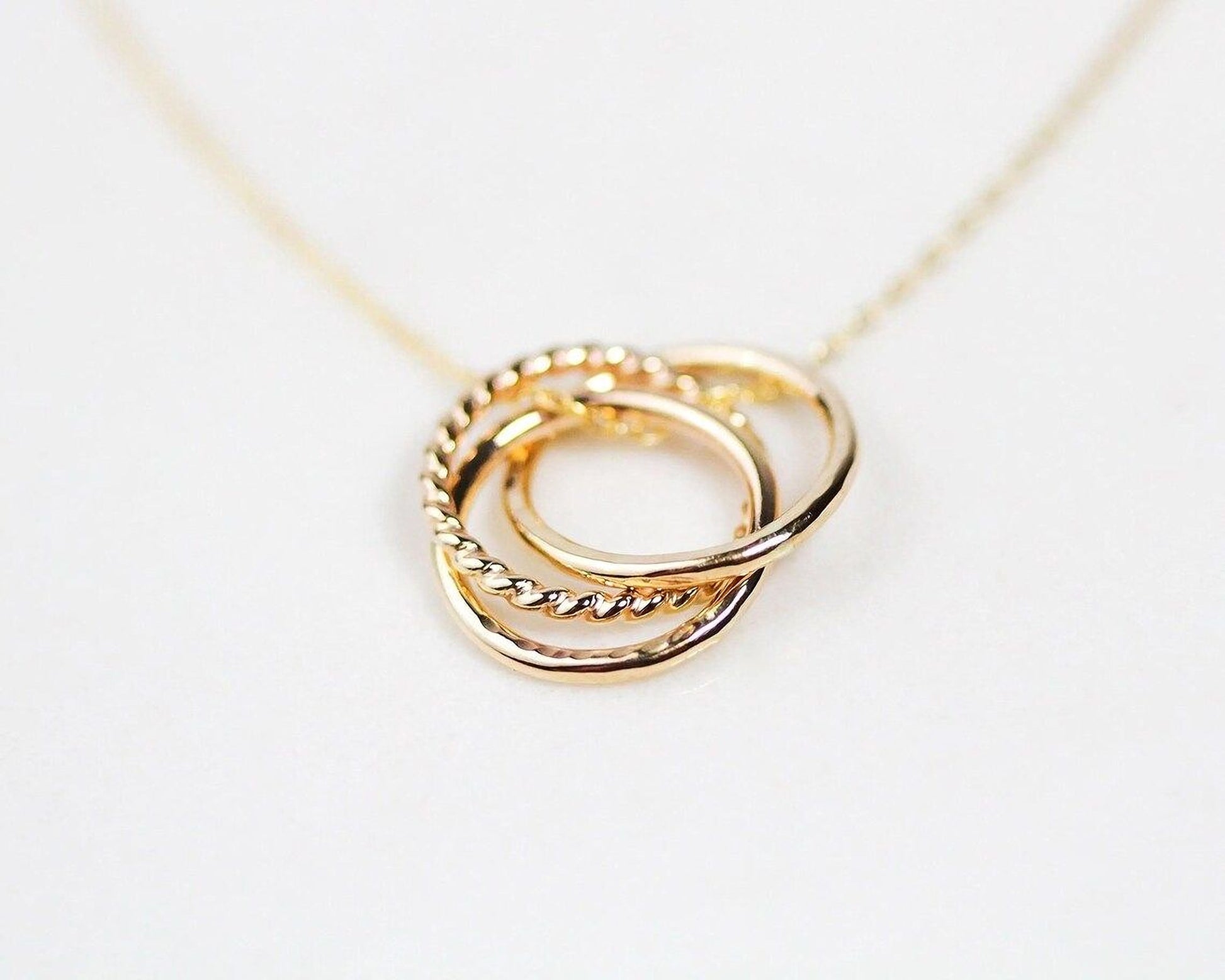 A close-up image of a gold necklace with a pendant featuring three intertwined rings.