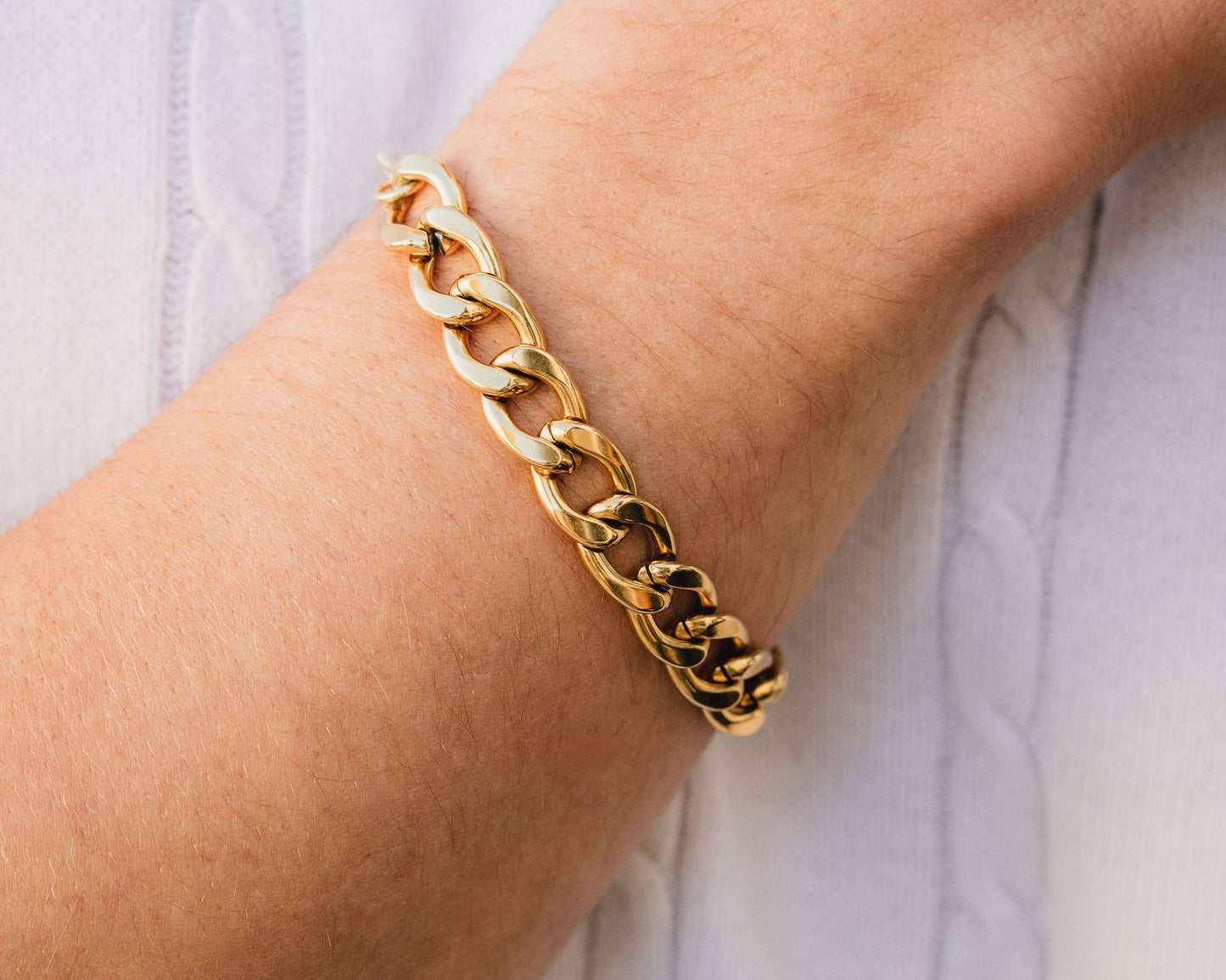 A gold chain bracelet is worn on a person's wrist.