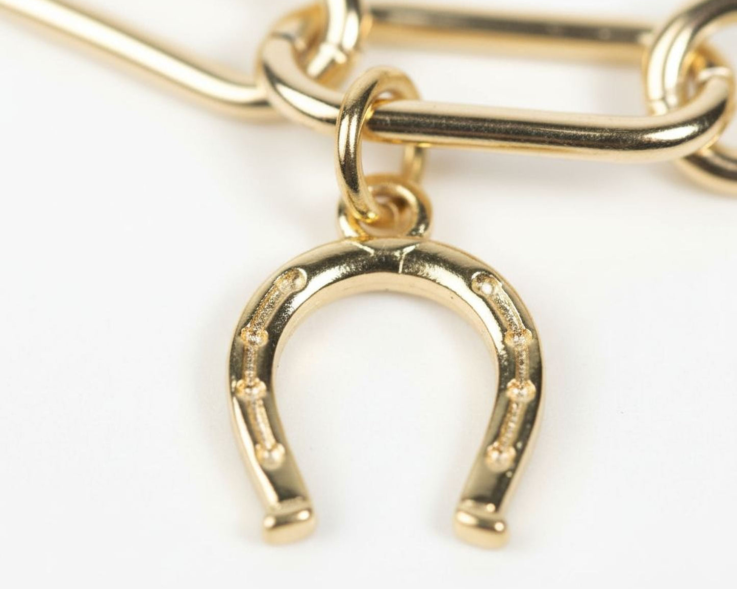 A close-up image of a gold-colored horseshoe charm with a chain attached to it.