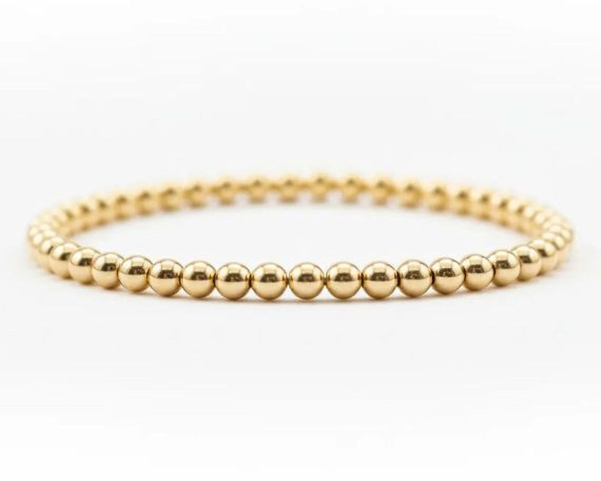 A gold-colored bracelet composed of numerous small, shiny gold beads arranged in a circular pattern.