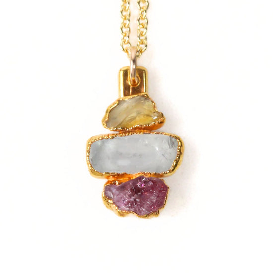 A necklace with a pendant featuring three different colored gemstones: a pale blue stone, a light yellow stone, and a deep purple stone.