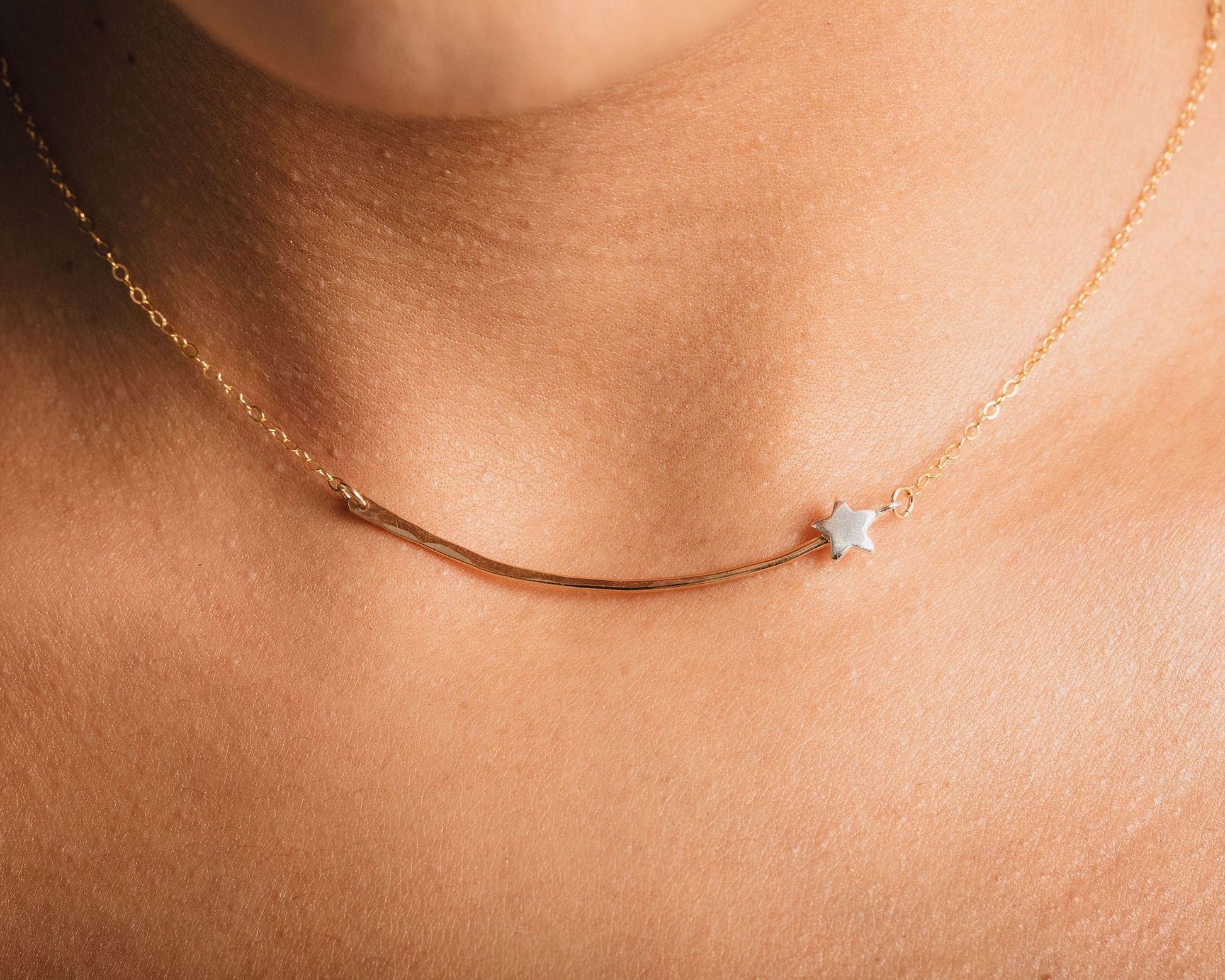 A close-up view of a delicate gold necklace with a small star charm on a curved metal bar.