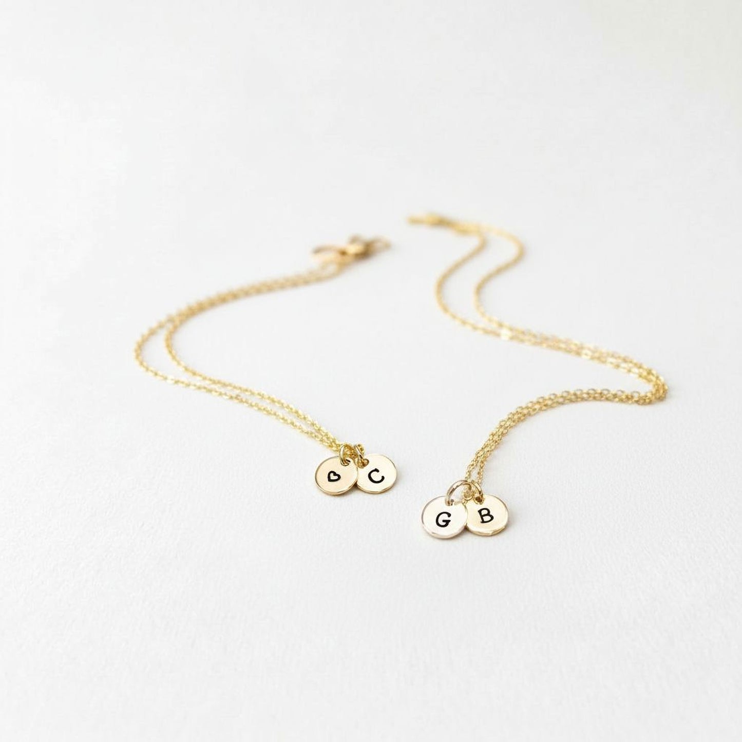A pair of gold-colored necklaces with small charms attached, each containing a letter.