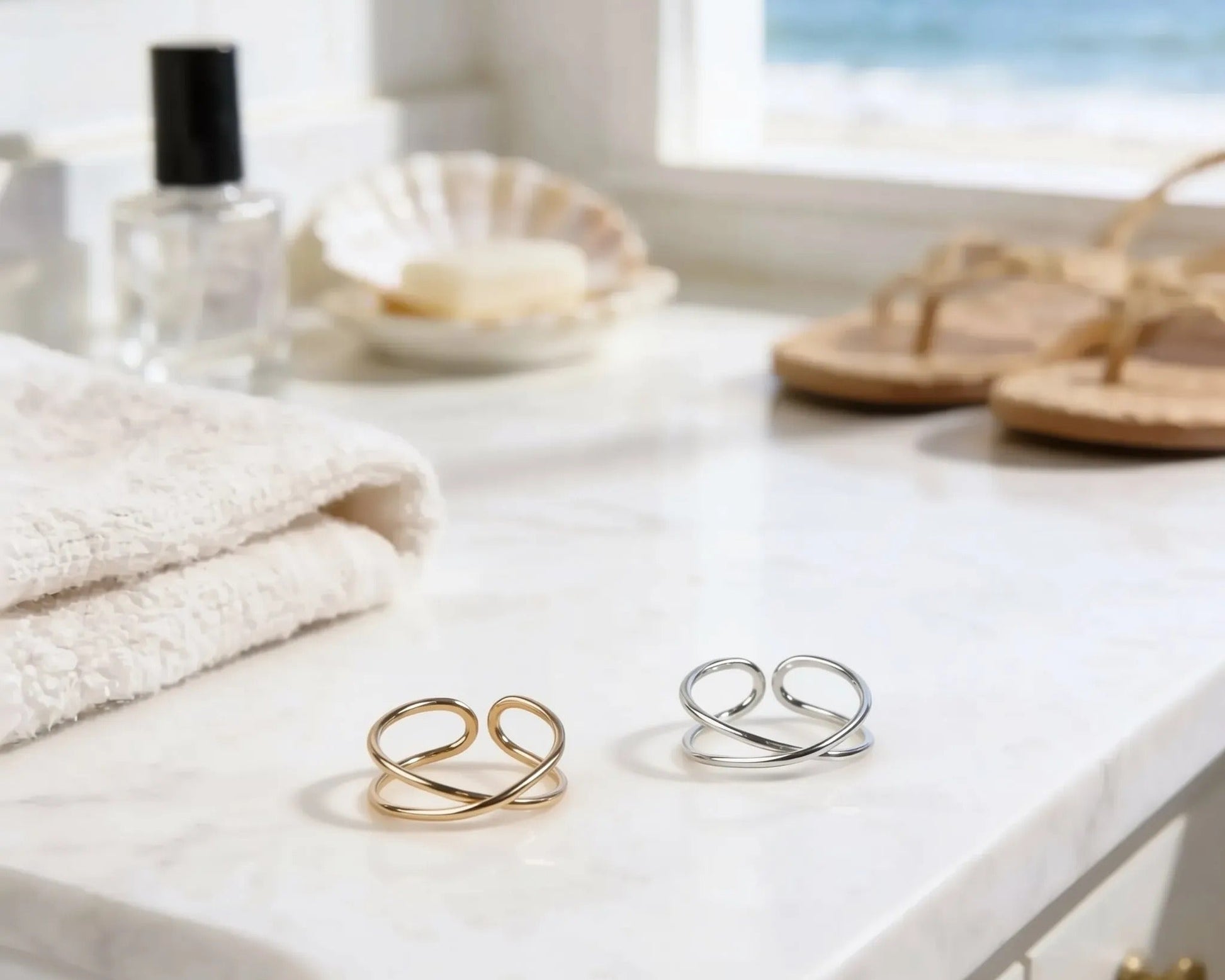 a bathroom counter with various items, including a pair of rings, a bottle of lotion, a seashell, and a pair of sandals, all placed on a white marble countertop.