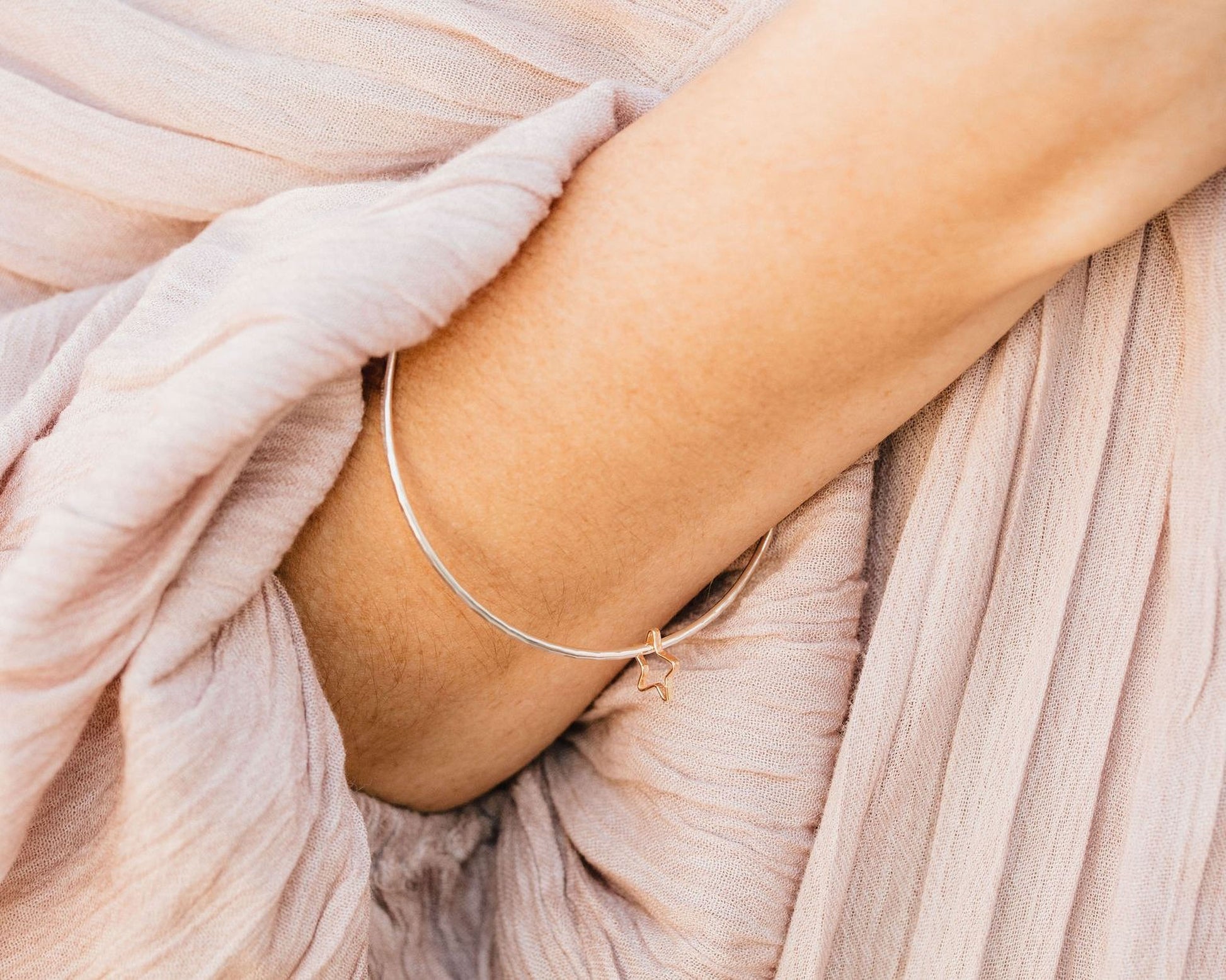 A close-up view of a person's arm wearing a silver bracelet with a charm.