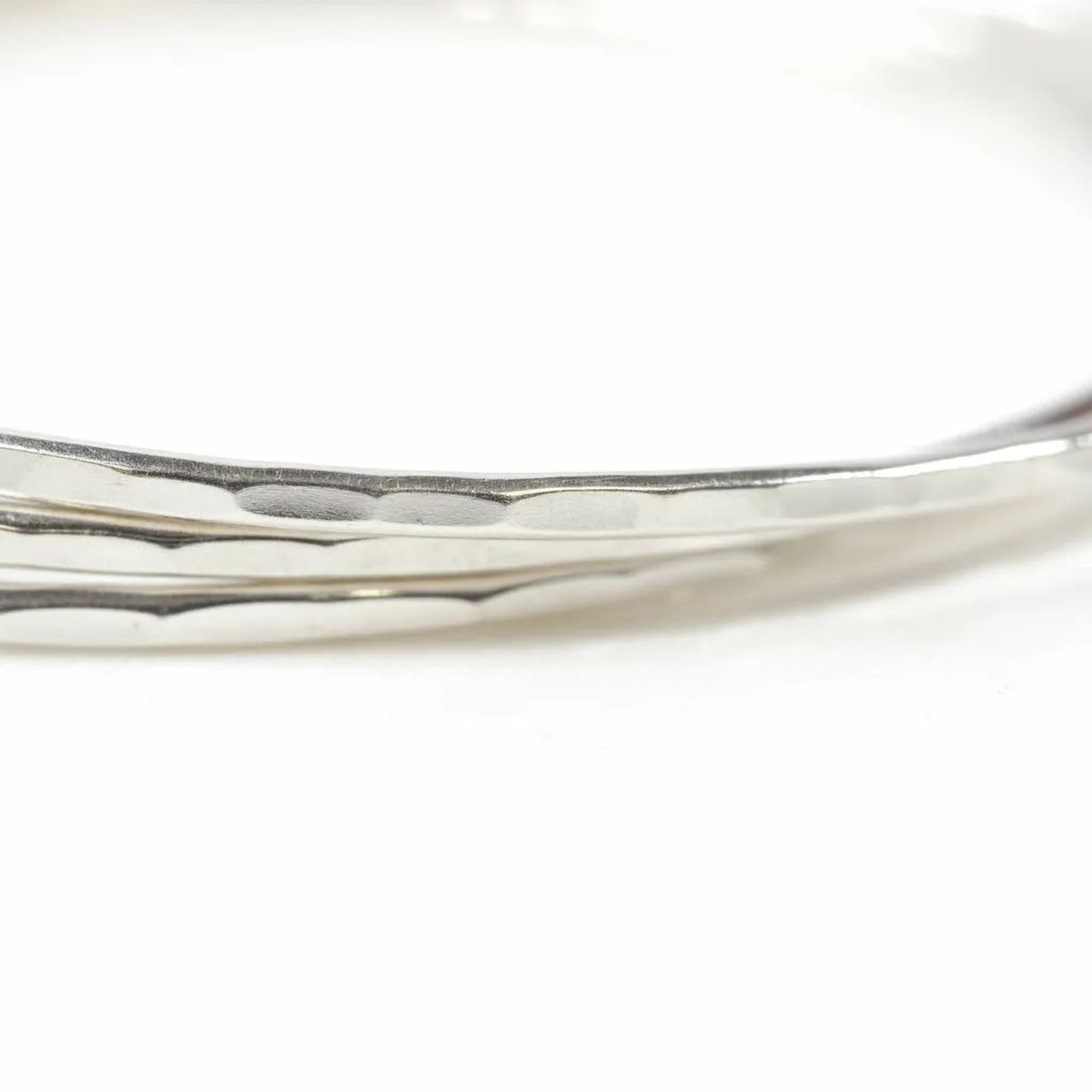 A close-up view of a silver bracelet with a textured surface, resting on a white background.
