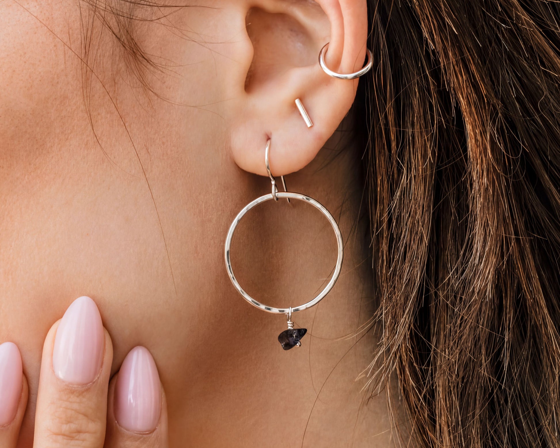 A close-up of a person's ear adorned with a pair of silver hoop earrings and a small stone accent.