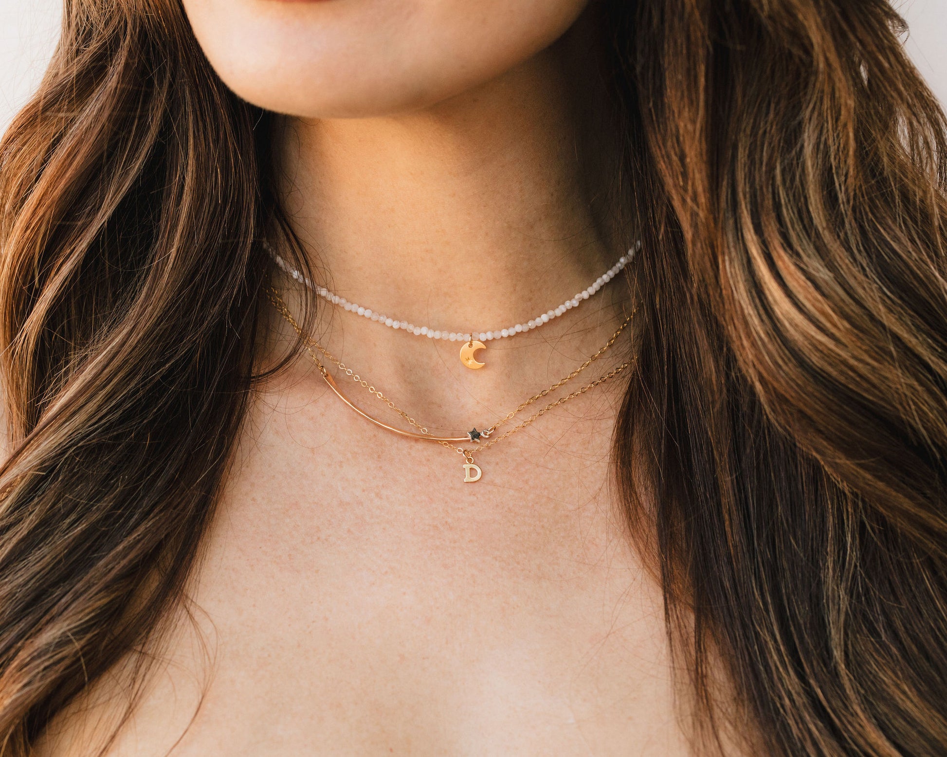A close-up view of a woman's neck adorned with multiple necklaces, including a pearl necklace, a charm necklace, and a chain necklace.