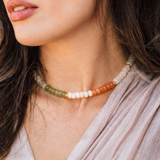 A close-up of a woman's neck and chest area, featuring a colorful beaded necklace with green, white, and orange beads.
