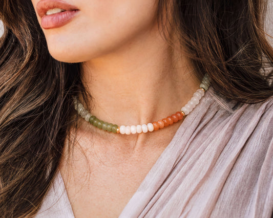 A close-up of a woman's neck and chest area, featuring a colorful beaded necklace with green, white, and orange beads.