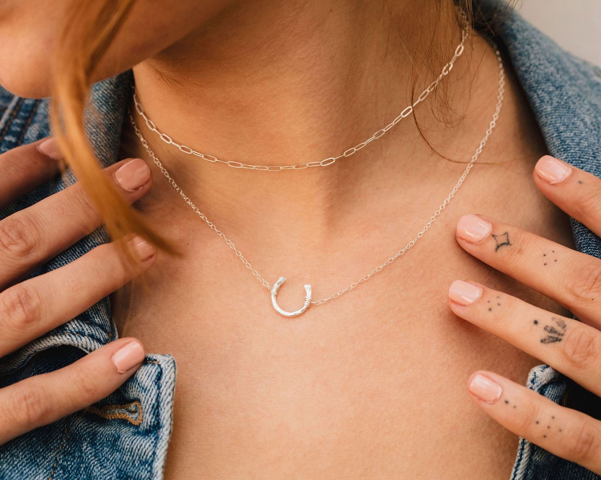 A close-up view of a person's neck and hands wearing a silver necklace with a small horseshoe pendant.