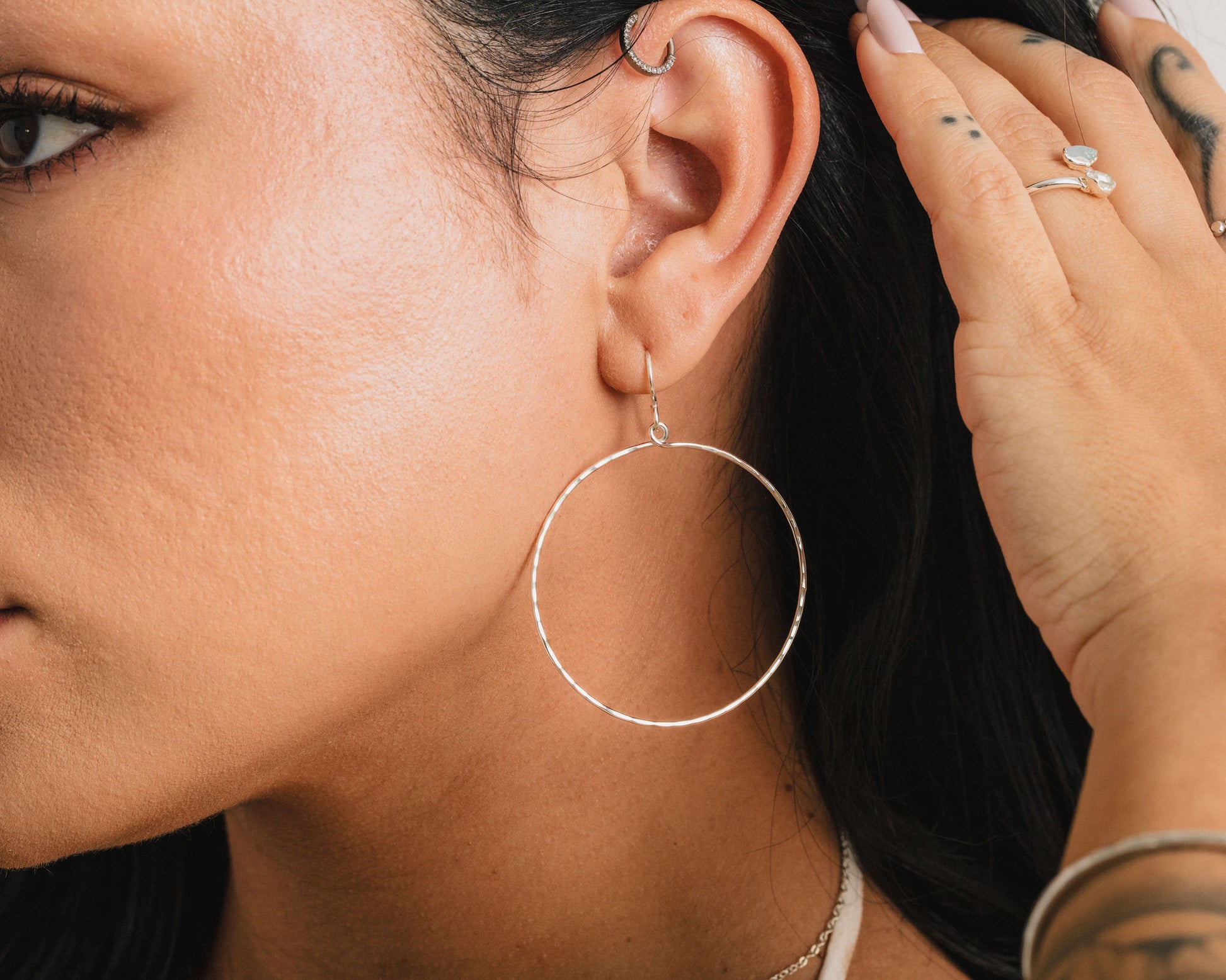 A close-up of a person's face, focusing on their earrings and hand.