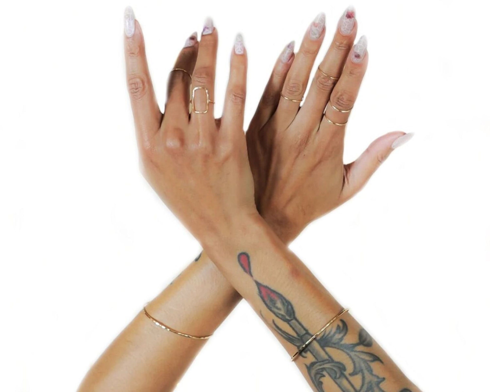 two hands with painted nails and tattoos, wearing rings on their fingers.