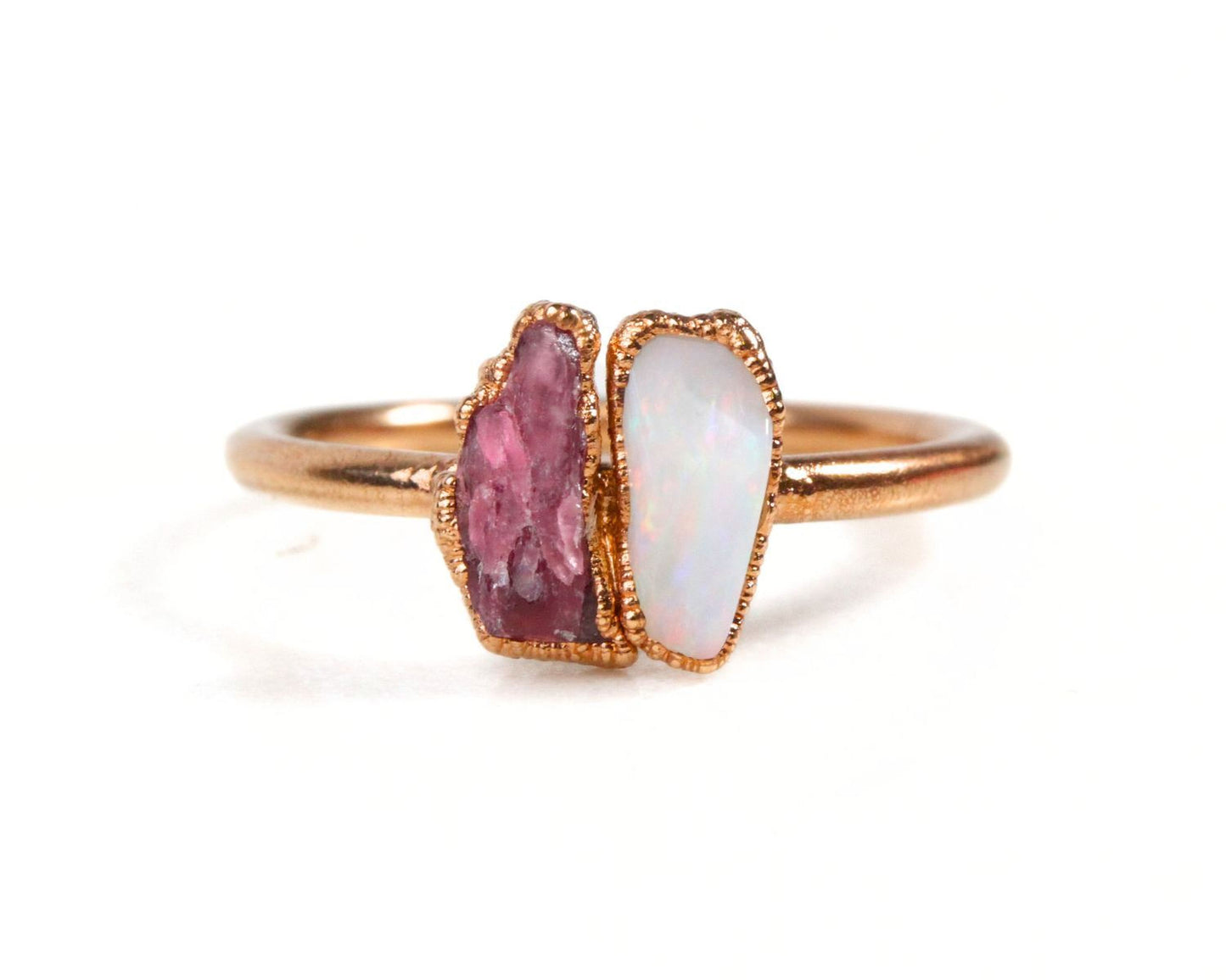 A gold ring with two gemstones, one pink and one white, set in the center.