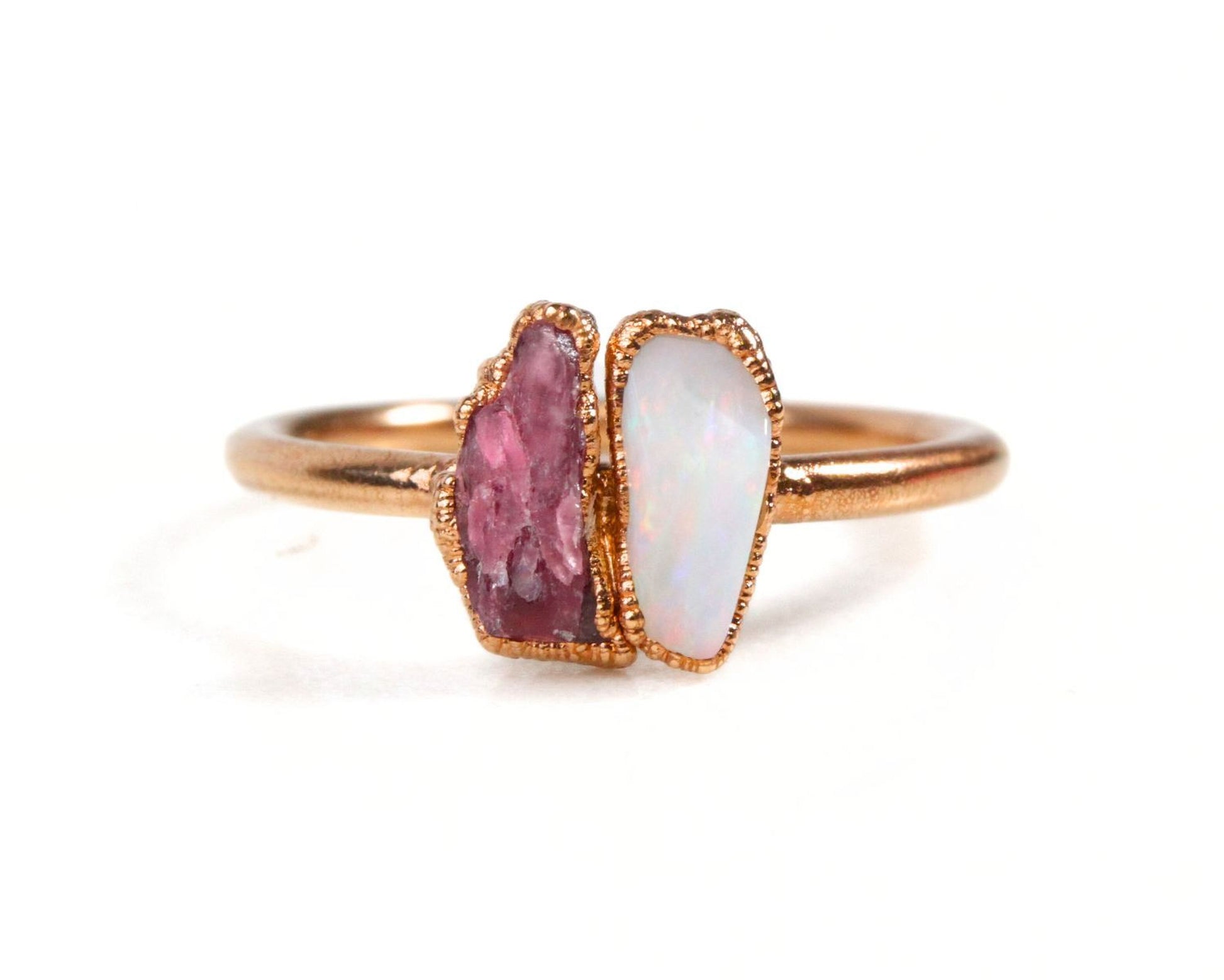 A gold ring with two gemstones, one pink and one white, set in the center.