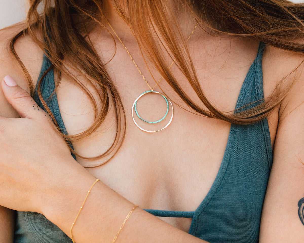 A close-up view of a person's chest and neck area, featuring a necklace with a circular pendant and a bracelet on their wrist.