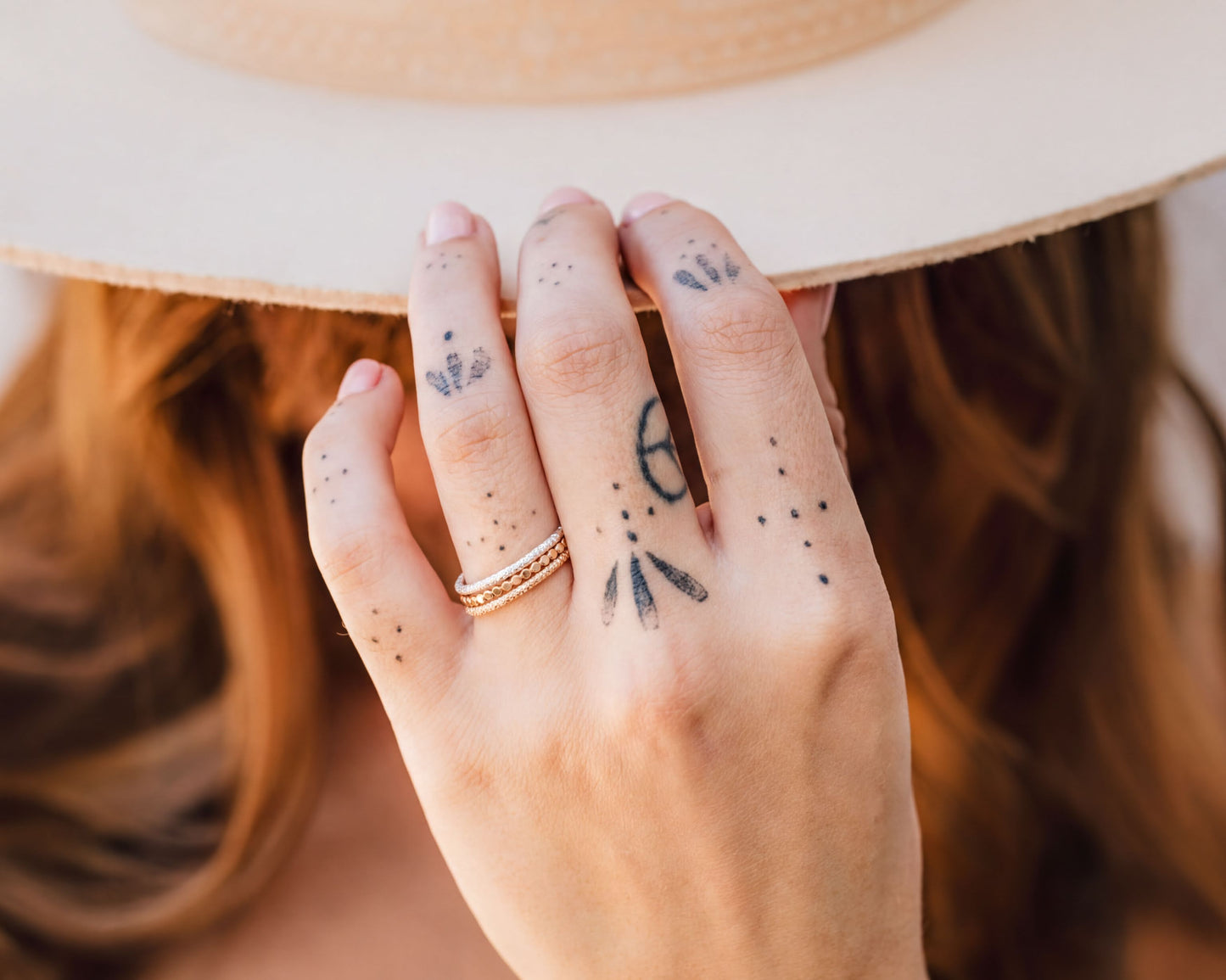 A close-up of a person's hand with tattoos on the fingers, wearing a white hat, and holding the hat over their head.