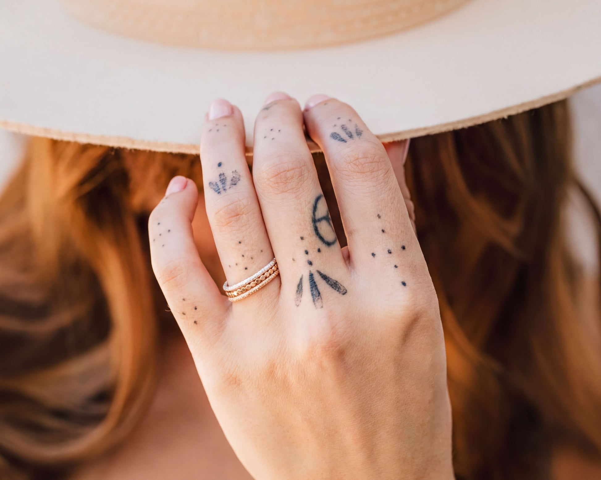 A close-up of a person's hand with tattoos on the fingers, wearing a white hat, and holding the hat over their head.