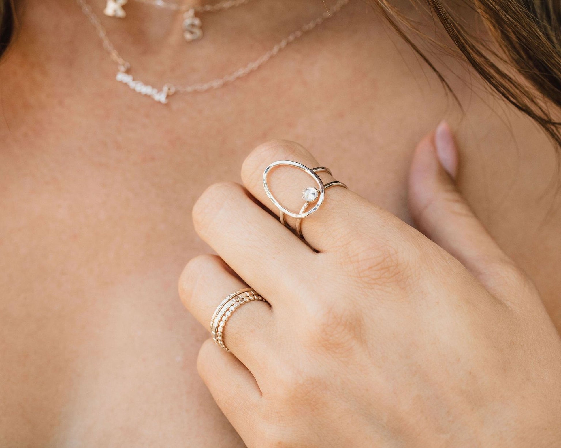 A close-up of a person's hand wearing multiple rings, including a ring with a small diamond and a ring with a unique circular design.