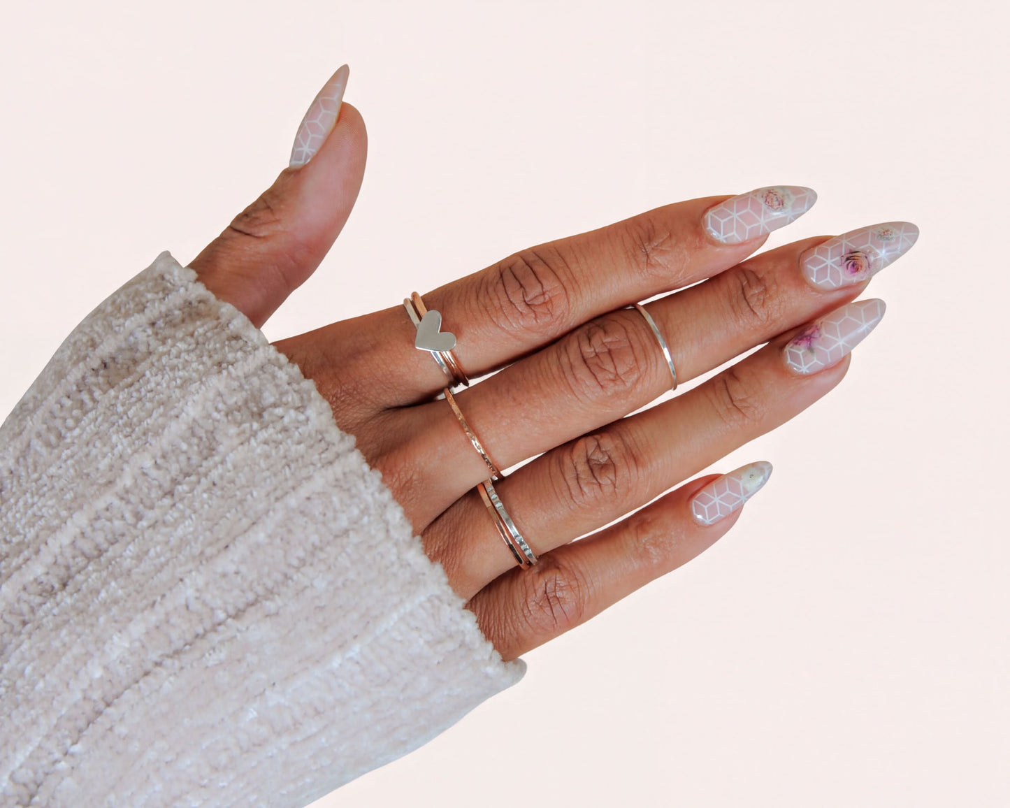 A close-up of a person's hand wearing multiple rings on their fingers, with their nails painted in a decorative pattern.