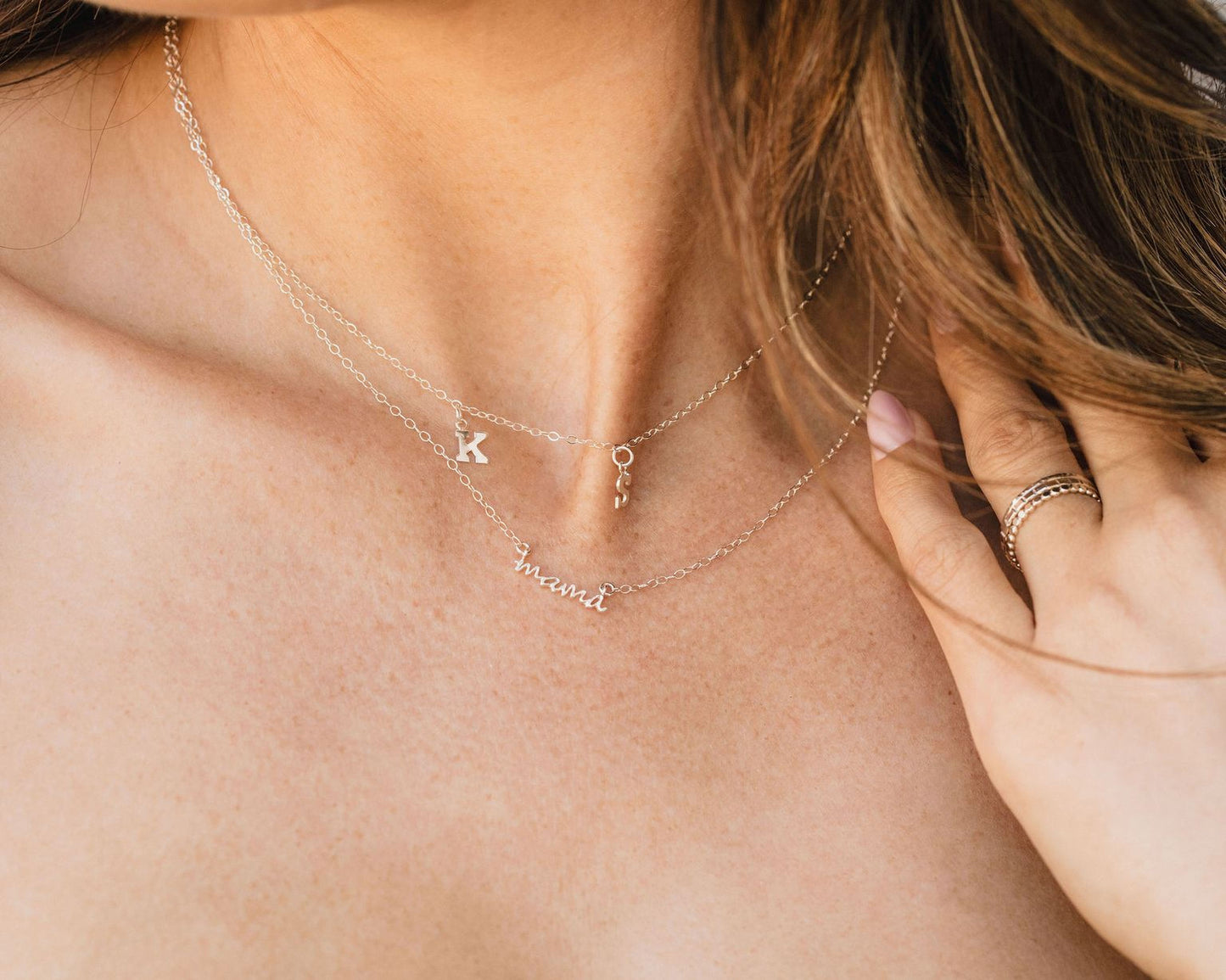 A close-up view of a person's neck and chest area, showing a necklace with a pendant and a ring on their finger.