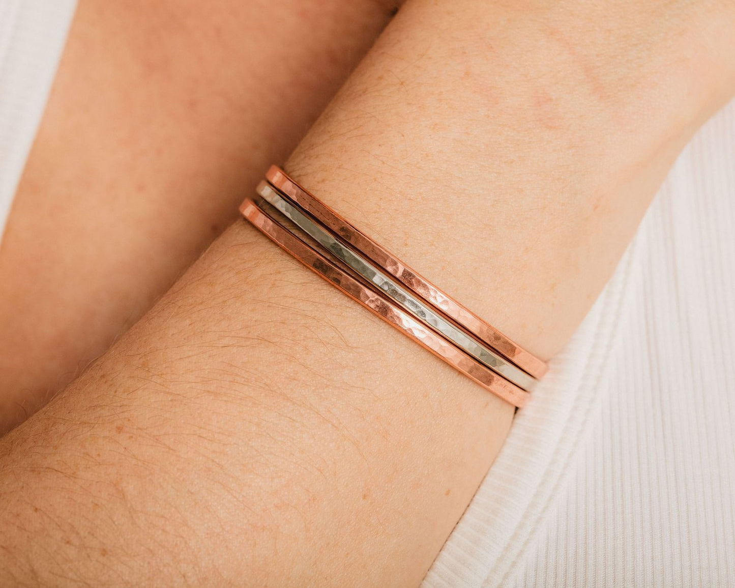 A close-up view of a person's arm wearing three overlapping copper-colored bracelets.