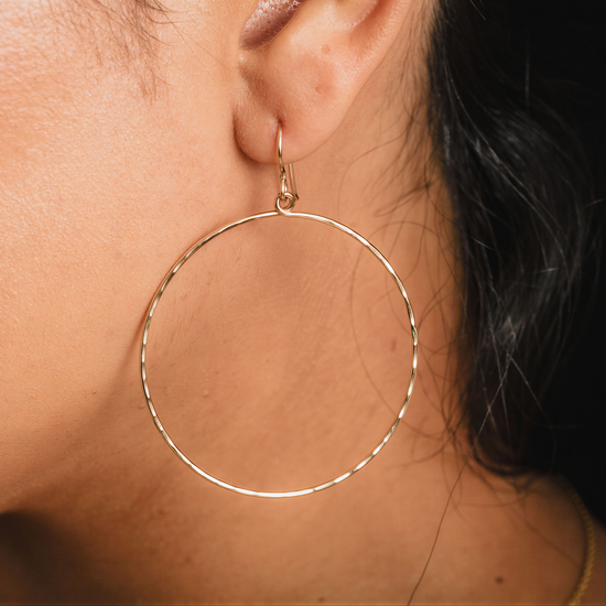 A close-up view of a person's ear wearing a large gold hoop earring.