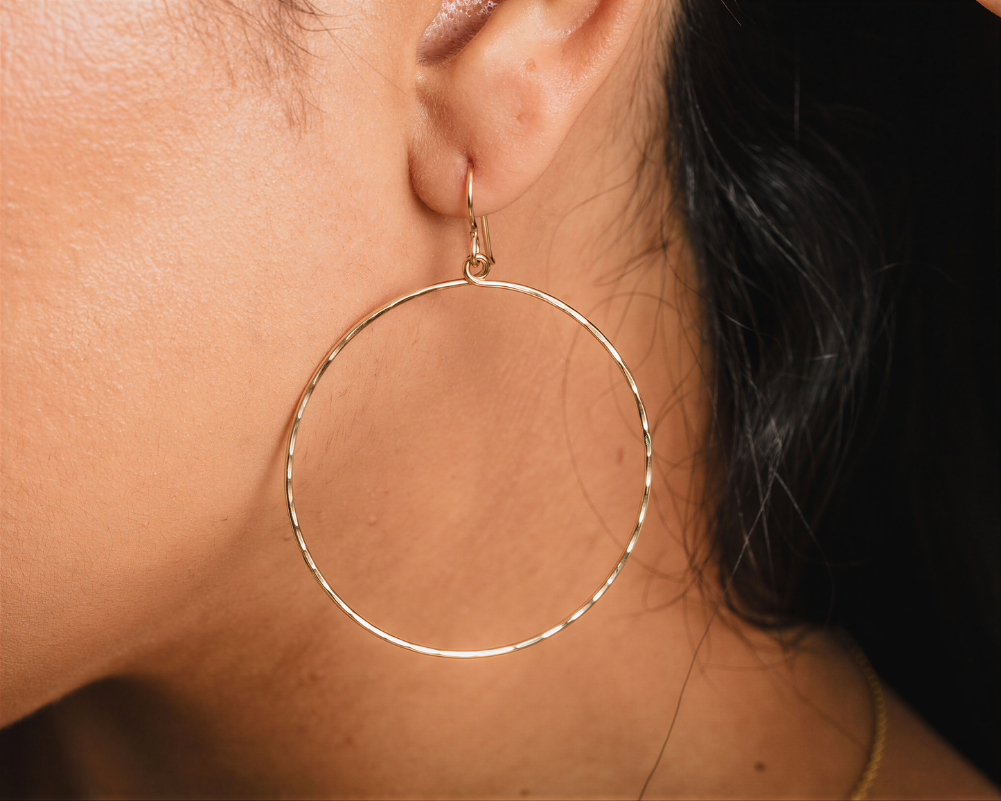 A close-up view of a person's ear wearing a large gold hoop earring.
