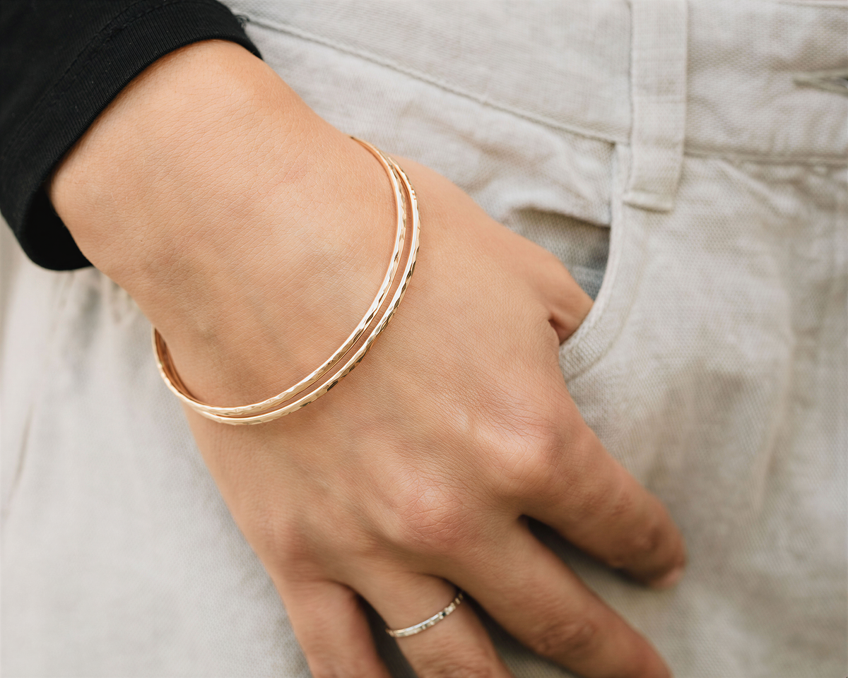 A close-up view of a person's hand wearing a gold-colored bracelet and ring.