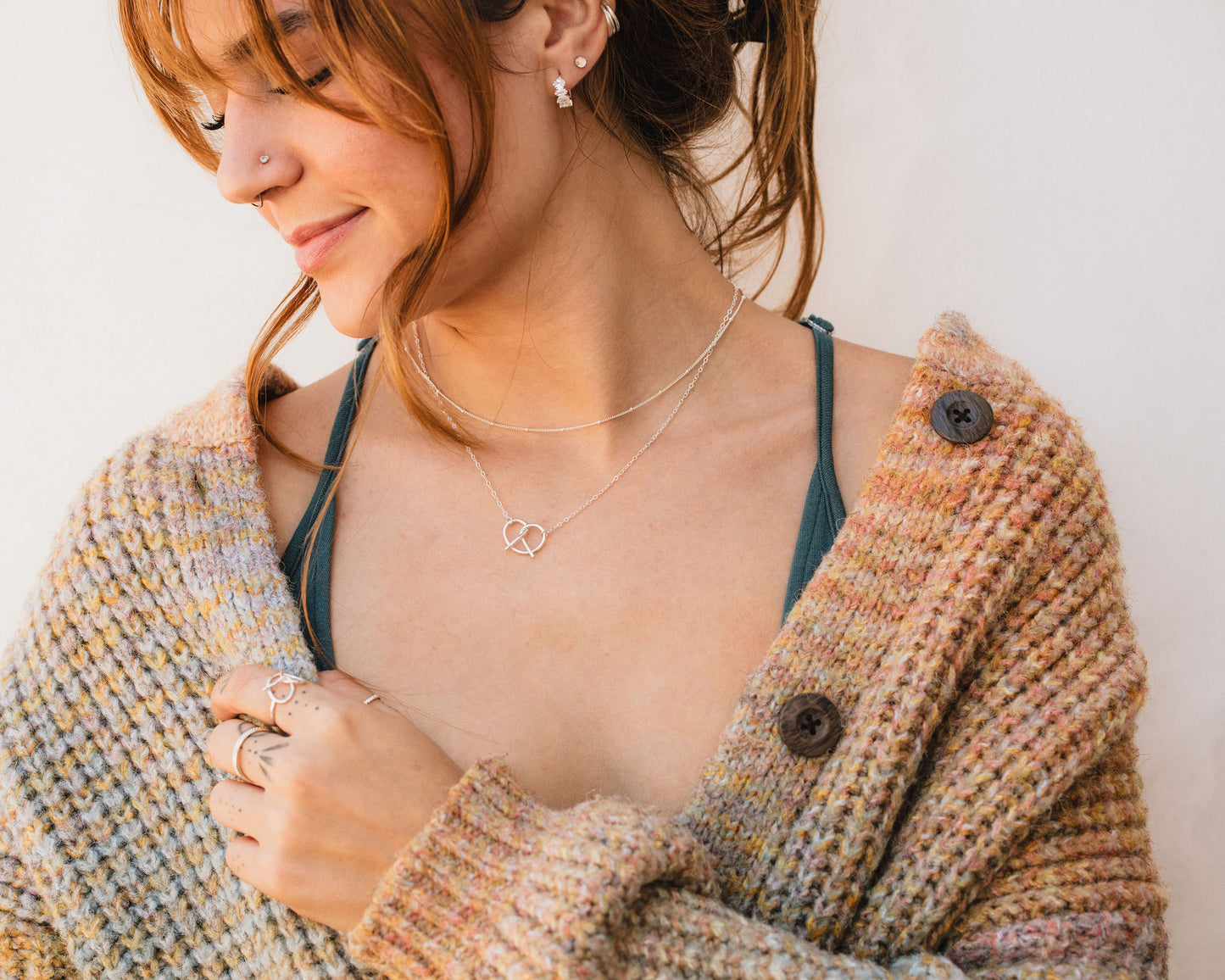 A woman with red hair wearing a brown cardigan and multiple rings on her fingers is smiling at the camera.