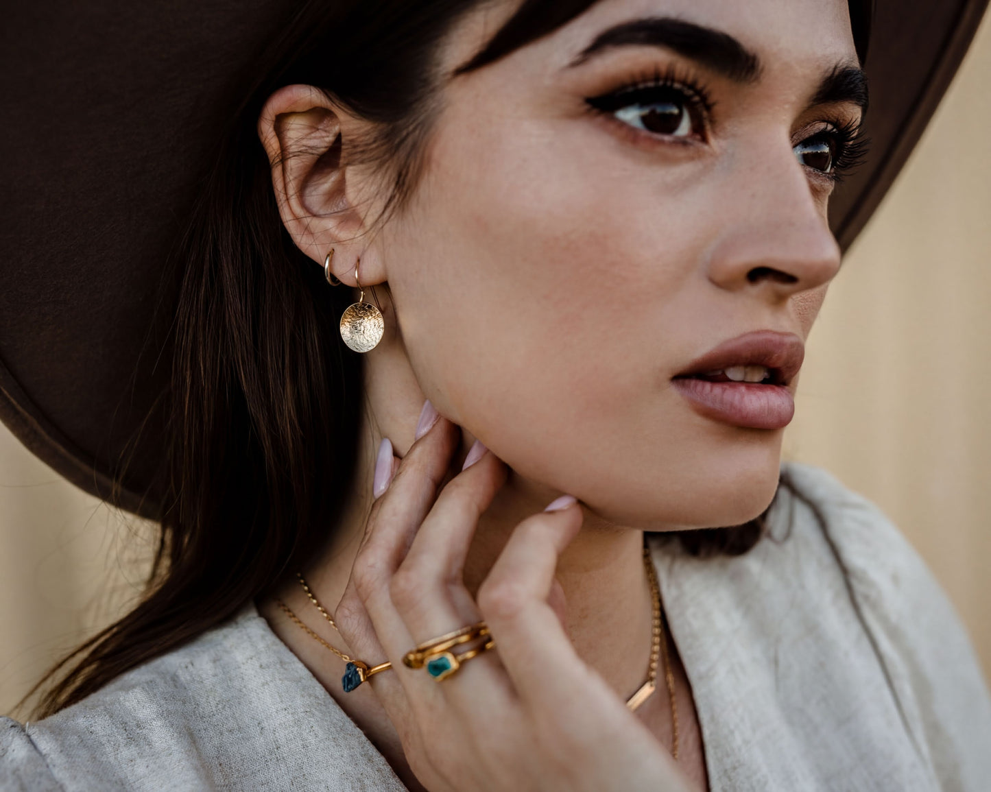 A close-up portrait of a woman wearing a large hat and multiple rings on her fingers, with a thoughtful expression on her face.