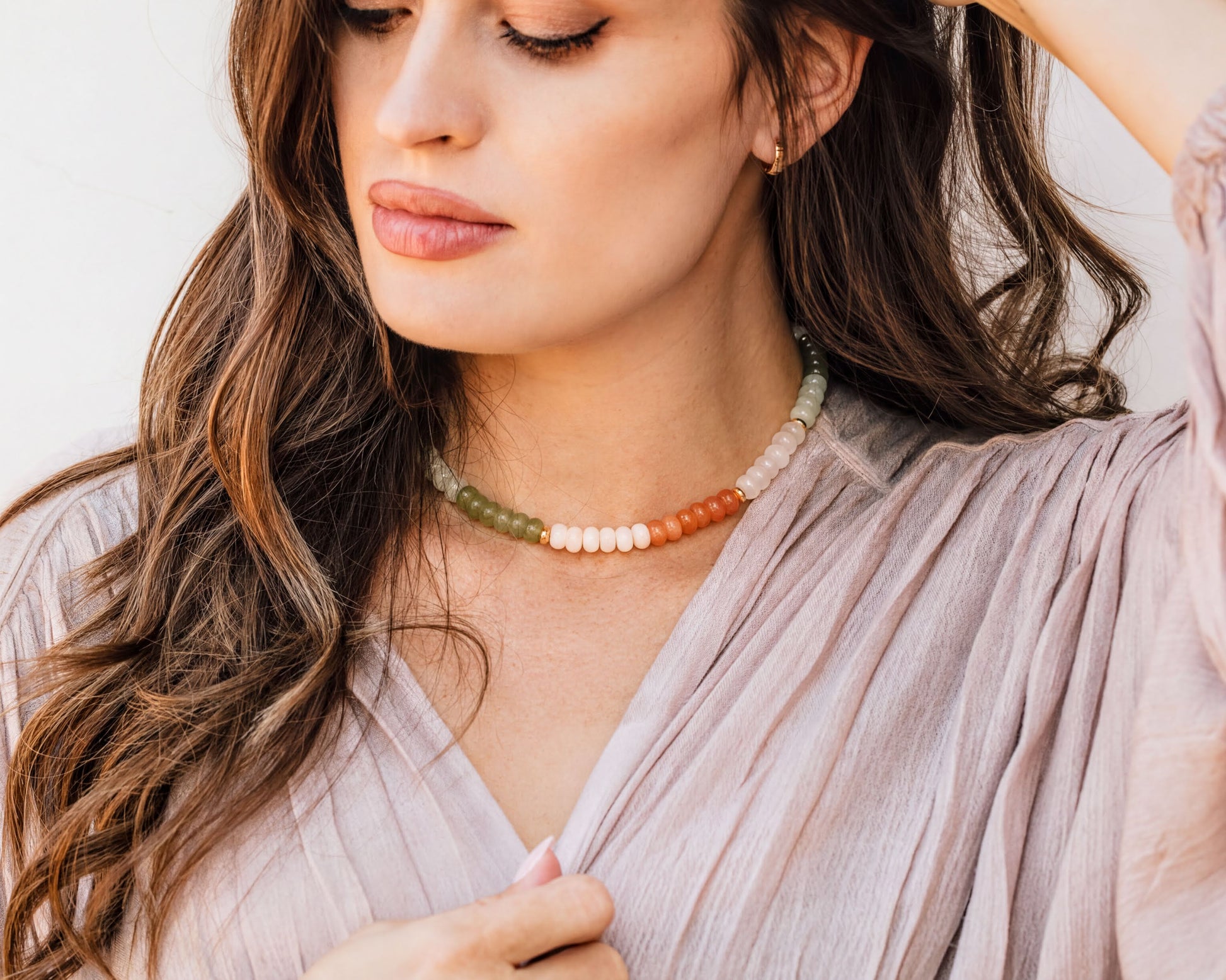 A woman with long, wavy brown hair wearing a necklace with colorful beads.
