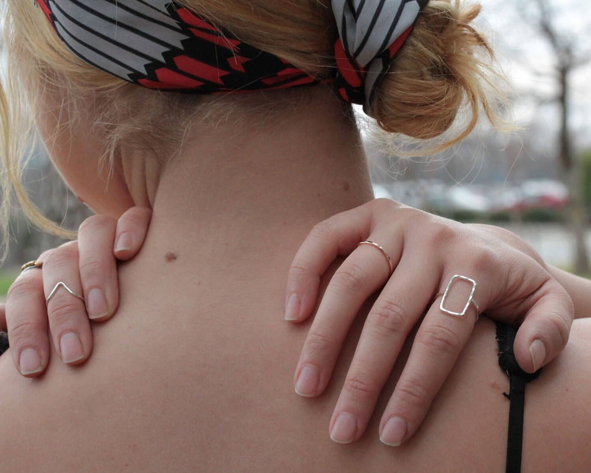 a close-up view of a person's back, focusing on their hand adorned with multiple rings and a ring on their finger.